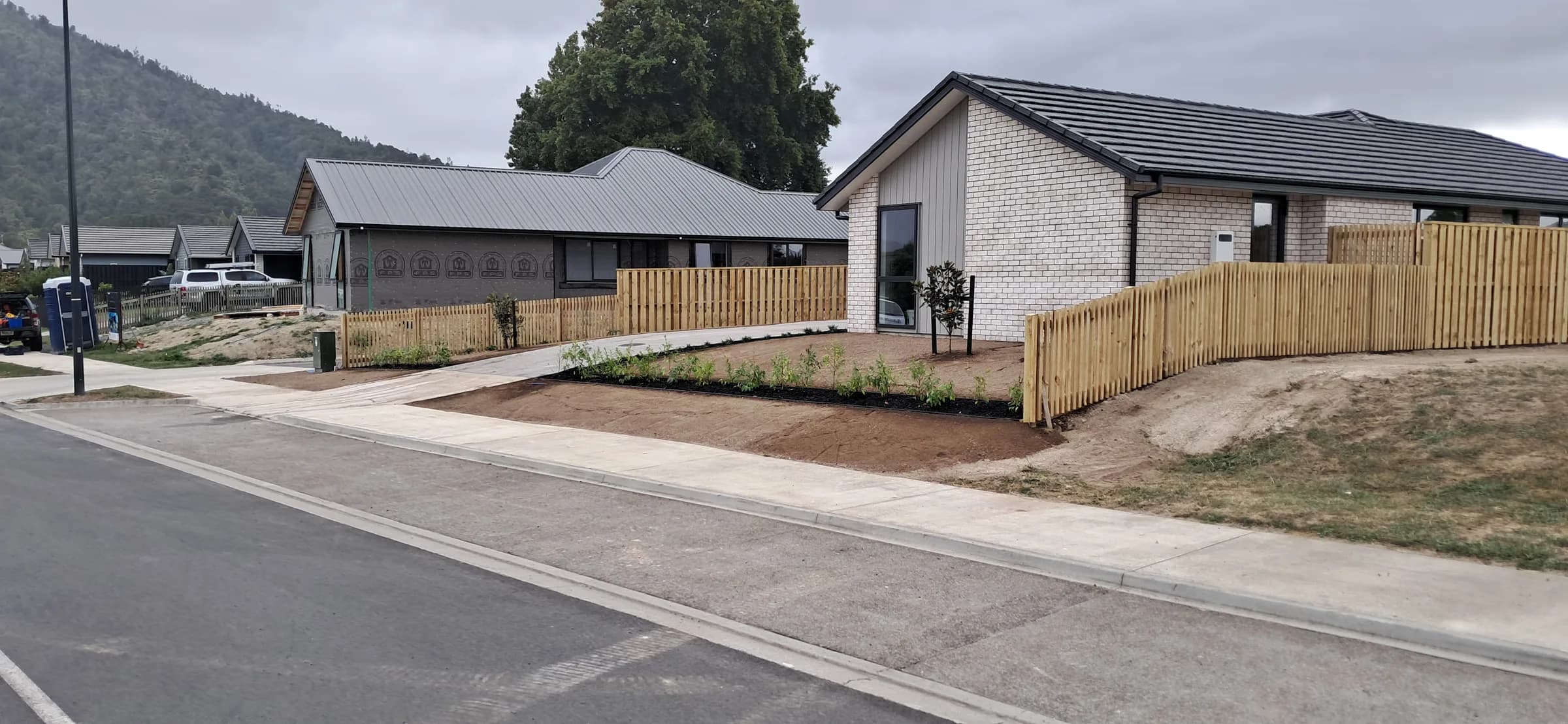 A new timber picket fence around a freshly landscaped new-build home in Hamilton, with neighbouring properties visible either side