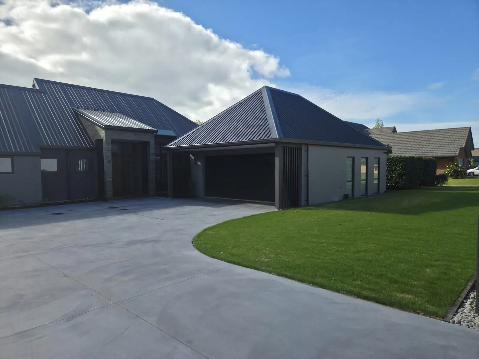 A finished concrete driveway curving from a Hamilton home to meet the road, crossing the footpath
