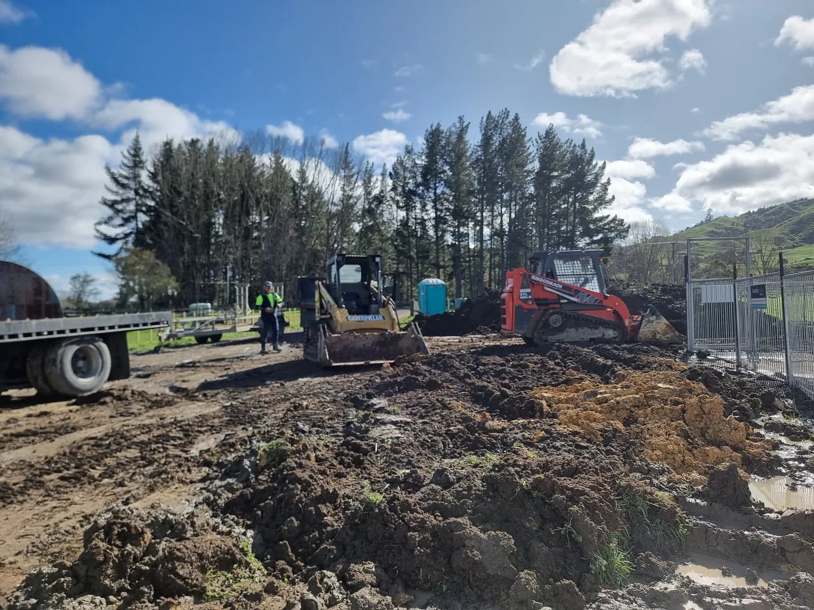 A skid steer and track loader moving stockpiled soil on an active Hamilton earthworks site, fence going in behind them